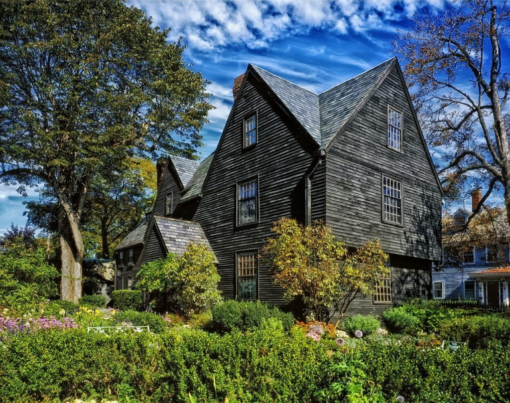 A wooden grey house surrounded by lush green trees in Salem, Massachusetts for a Halloween trip destination. 