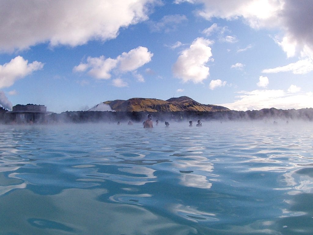 A large group of people relaxing in the Blue Lagoon hot spring in Iceland with the lava field in the background. 