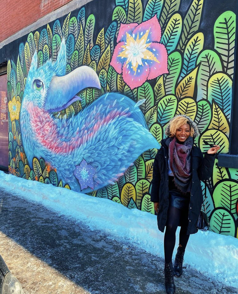 Black girl wearing a winter jacket in front of a color mural. 