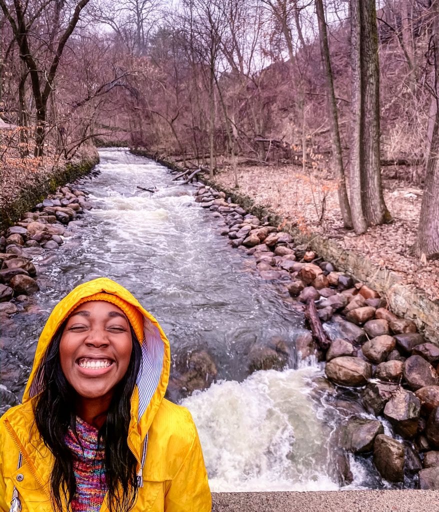 Black girl wearing yellow hat and yellow raincoat by the stream.