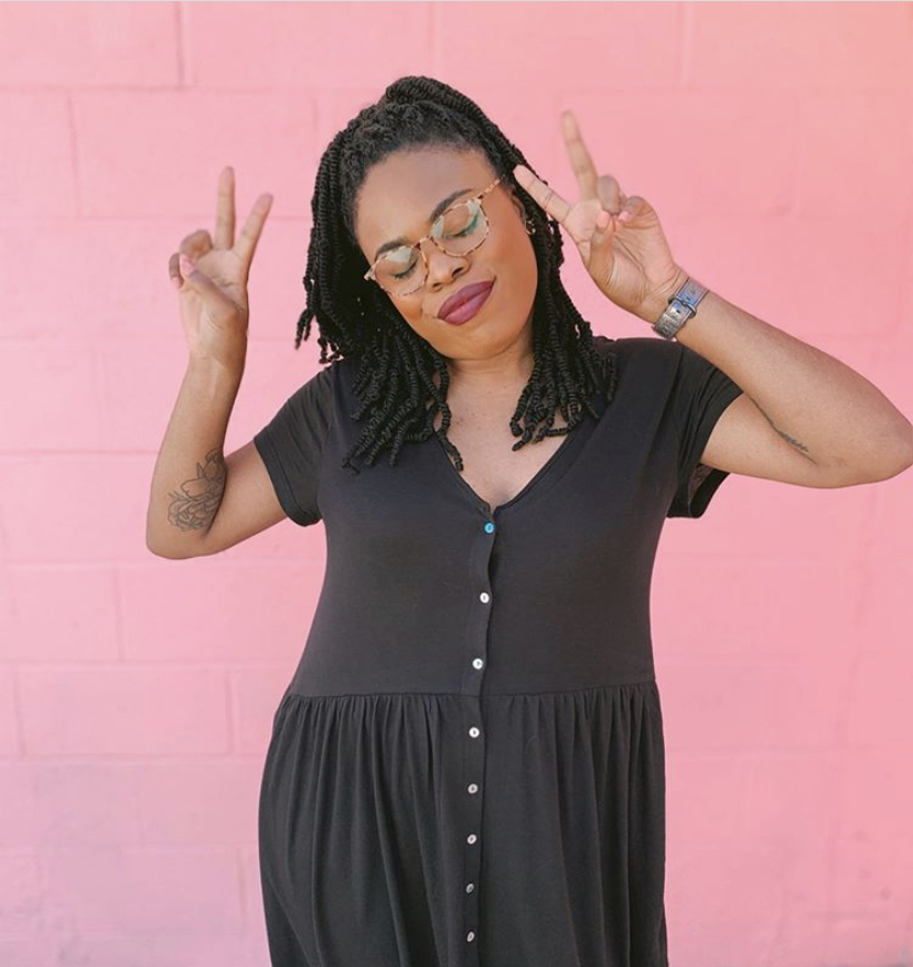 Black girl throwing up peace signs in front of a pink background. 