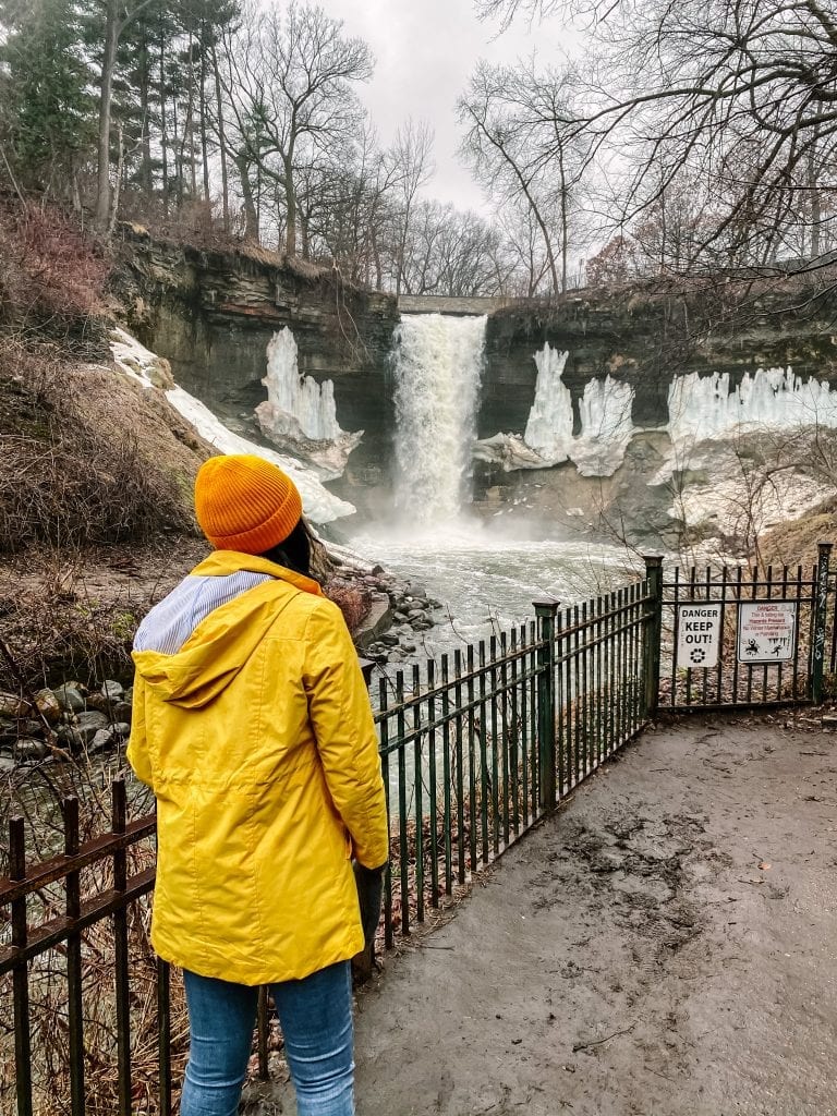 Girl in yellow jacket standing in front of Minnehaha Falls in Minnesota