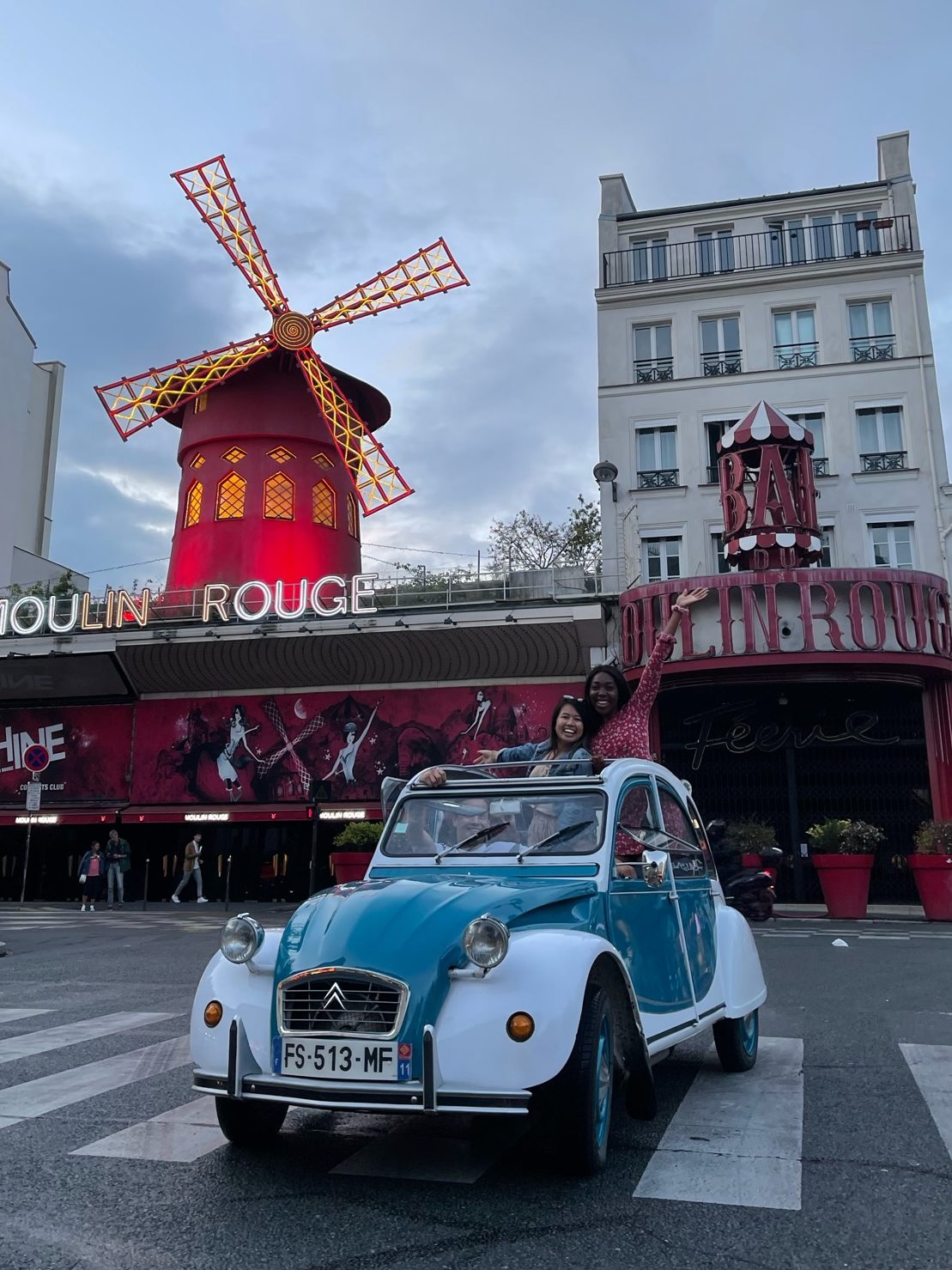 two girls standing out of a car in front of the Moulin Rouge Building in Paris, France