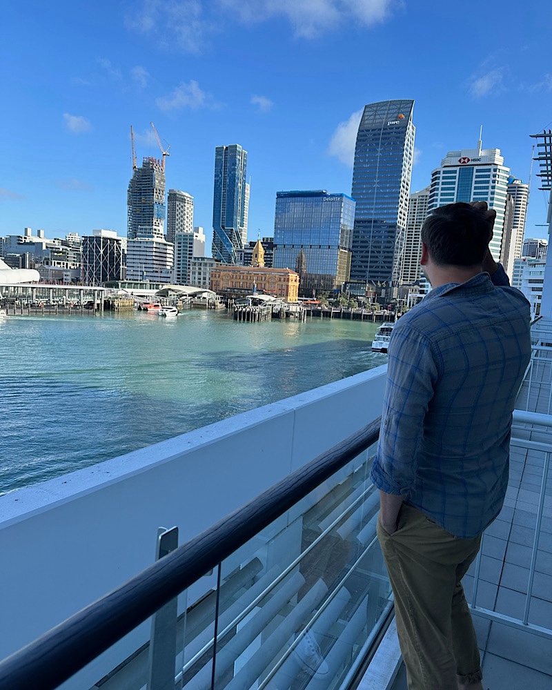 man staring out at the harbor in Auckland New Zealand. City buildings in the background 