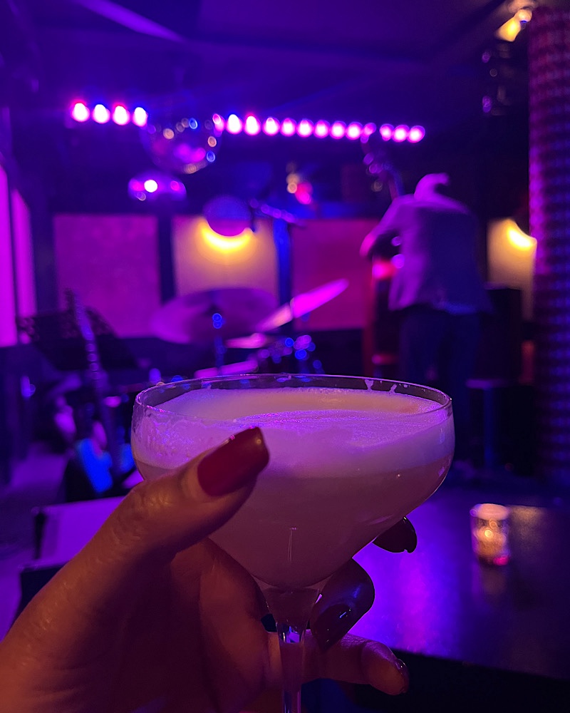 someone holding a cocktail with a jazz band in the background