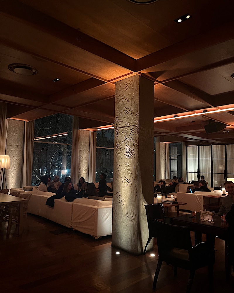 Dim lit room showcasing people sitting on white couches inside the Public Hotel lounge and bar 